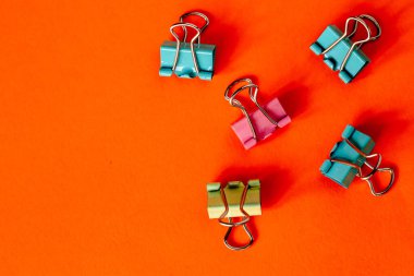 Turuncu arka planda renkli ataçlar. Boşluğu kopyala.