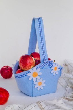 Beyaz arka planda beyaz papatyalar olan mavi keçeli sepetteki tatlı kırmızı elmalar. Yan görüş. Sağlıklı yaşam tarzı kavramı.