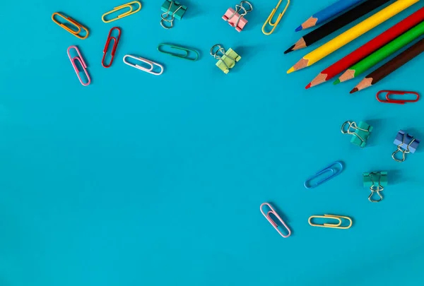 Many colored pencils and paper clips on a blue background. Copy space.