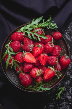 Kahverengi tabakta taze kırmızı çilekler ve koyu peçeteli yeşil roka..