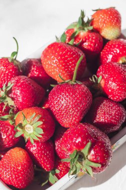 Beyaz bir kasede, parlak bir güneş ışığında kırmızı çilekler..