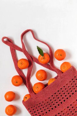 Beyaz bir arka planda, tığ işi örgü ören bir çantada taze mandalinalar. Üst Manzara. Boşluğu kopyala.