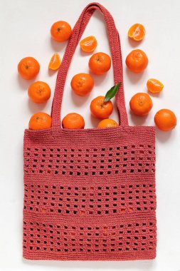 Beyaz arka planda kırmızı örgü örülü eko poşette taze mandalinalar. Üst görünüm.