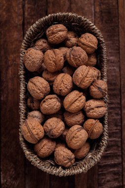 Tüm organik cevizleri oval hasır sepetin içinde koyu ahşap bir arka planda..