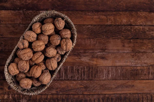 Koyu ahşap bir arka planda oval hasır sepetin içinde ceviz. Boşluğu kopyala.