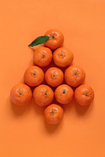 Fresh organic clementines in Christmas tree shape on an orange background. Copy space. Creative concept.