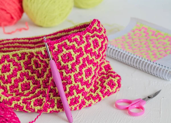 The process of creating a knit bag with a bright ethnic geometric pattern. Pink yellow crochted texture. Creative working concept.