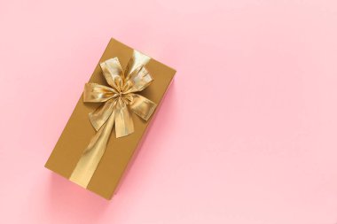 Golden gift box with golden ribbon and bow on a pink background. Top view. Copy space.