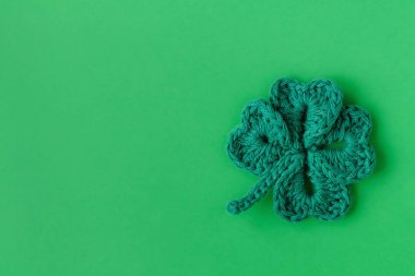 St. Patrick's day decoration. Green crochet shamrock or clover leaf on a green background. Top view. Copy space.