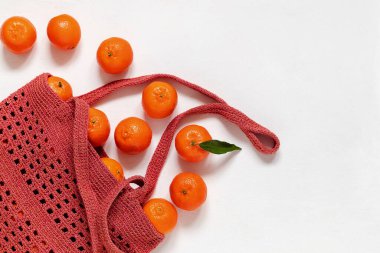 Fresh tangerines in a crochet shopping bag on a white background. Top view. Copy space.