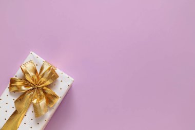 White gift box with golden ribbon and bow on a light purple background. Top view. Copy space.