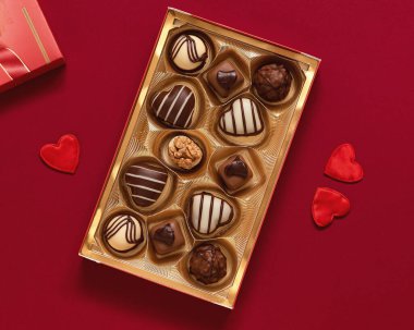 Box with chocolate pralines and red heart decoration for Valentine's Day on a burgundy background.