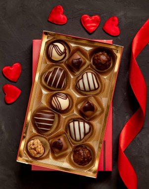 Gift box with chocolate pralines, red ribbon and heart shaped decoration for Valentine's Day on a grey background. Top view.