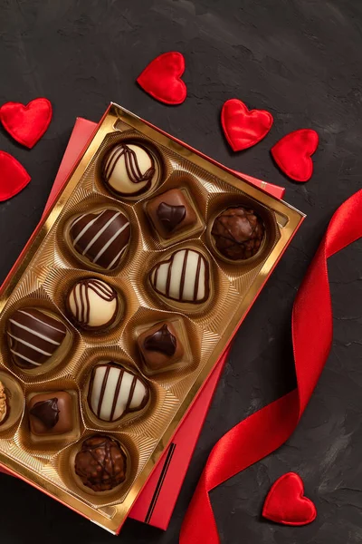 Gift box with chocolate candies, ribbon and red heart decoration for Valentine's Day on a grey background. Top view.