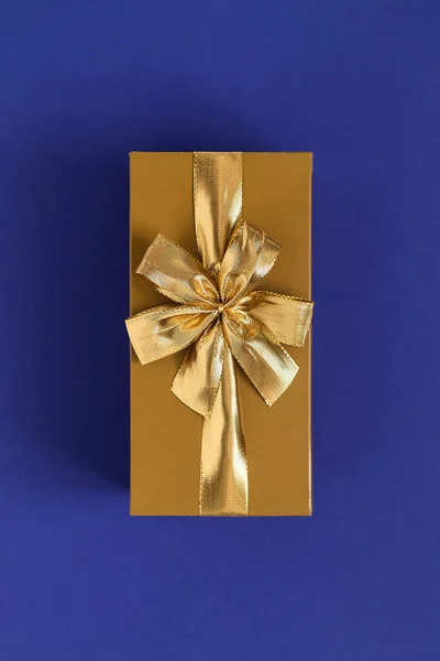 Golden gift box with golden ribbon and bow on a blue background. Top view.