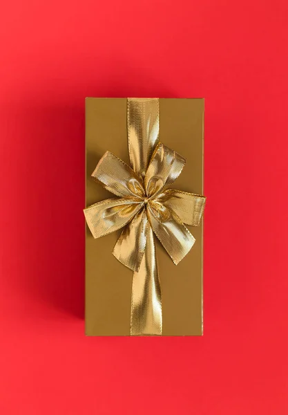 Golden gift box with golden ribbon and bow on a red background. Top view. Copy space.