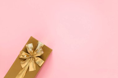 Golden gift box with golden ribbon and bow on a pink background. Top view. Copy space.