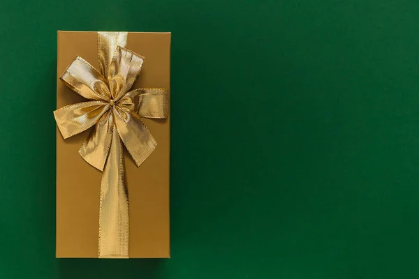 Golden gift box with golden ribbon and bow on a green background. Top view. Copy space.