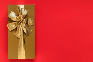 Golden gift box with golden ribbon and bow on a red background. Top view. Copy space.