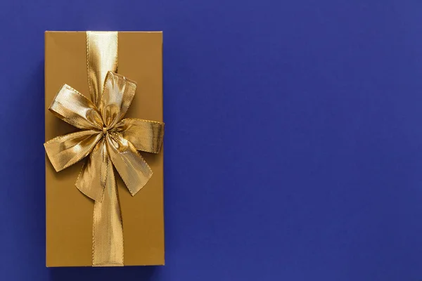 Golden gift box with golden ribbon and bow on a blue background. Top view. Copy space.