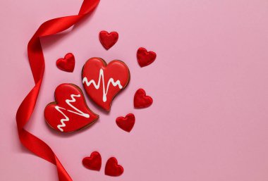 Red heart shaped gingerbread and red satin ribbon on a pink background. Love concept. Copy space.
