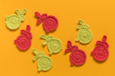 Easter background with red and yellow crochet bunnies. Easter decoratin on a yellow backgound. Top view.