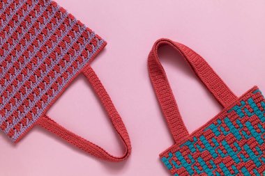 Pembe arka planda mozaik desenli iki tığ işi market çantası. Sıfır atık ve çevre dostu alışveriş kavramı.
