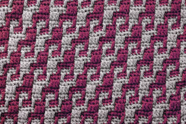 Texture of crochet fabric with burgundy grey geometric pattern. Mosaic crochet background.