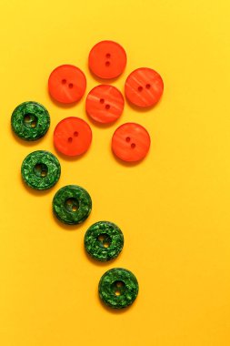 Sarı arka planda turuncu ve yeşil plastik düğmelerden yapılmış Daisy çiçeği. Üst Manzara. Boşluğu kopyala.
