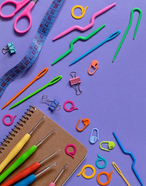 Notebook and colorful knitting tools on a purple background. Top view. Copy space.