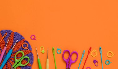 Parlak tığ işi aletler ve turuncu arka planda tığ işi çiçek altlığı. Üst Manzara. Boşluğu kopyala.