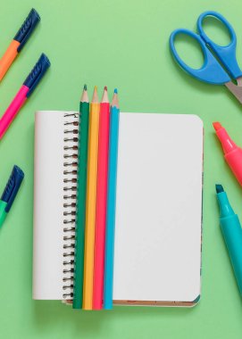 Not defteri, renkli kalemler yeşil arka planda kalemler, kalemler ve makas. Okul konseptine dönelim..