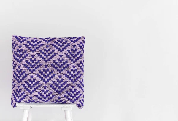 白い壁に椅子に抽象的なモザイクパターンを持つ手作りの青いかぎ針編みの枕 スペースのコピー — ストック写真