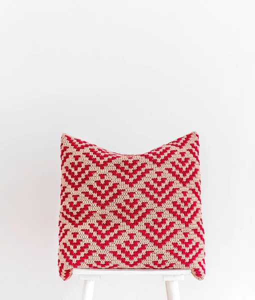 白い壁に向かって椅子に赤い手作りのかぎ針編みの枕 抽象的なモザイクパターンのかぎ針編みの枕 スペースのコピー — ストック写真
