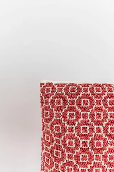 白い壁に対する抽象的な民族パターンを持つかぎ針編みの赤い枕 スペースのコピー — ストック写真