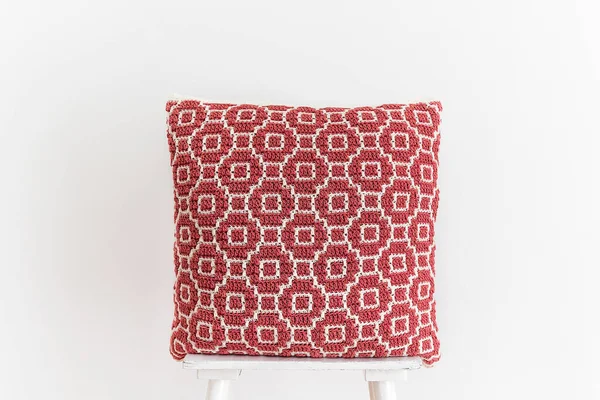 白い壁に対して椅子の上に抽象的なモザイクパターンを持つ柔らかい赤のかぎ針編みのクッション スペースのコピー — ストック写真