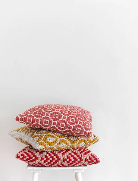 白い壁に対して椅子の上にかぎ針編みの枕を積ま 抽象的なモザイク模様の手編みの枕 — ストック写真