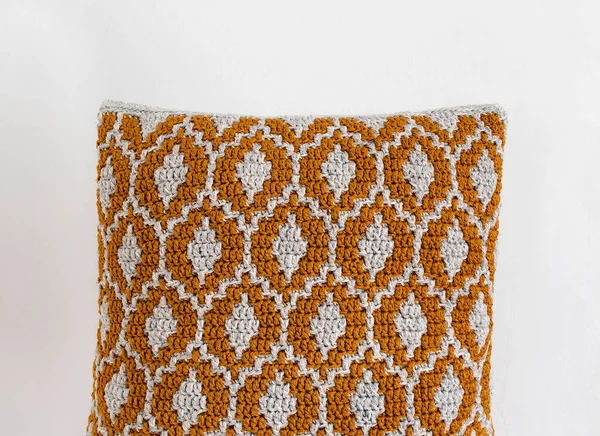 白い壁に抽象的な民族パターンとオレンジのかぎ針編みのクッション スペースのコピー — ストック写真