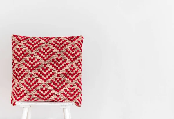 白い壁に椅子に抽象的なモザイクパターンを持つ手作りの赤いかぎ針編みの枕 スペースのコピー — ストック写真