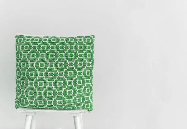 白い壁に椅子に抽象的なモザイクパターンを持つ手作りの緑のかぎ針編みの枕 スペースのコピー — ストック写真