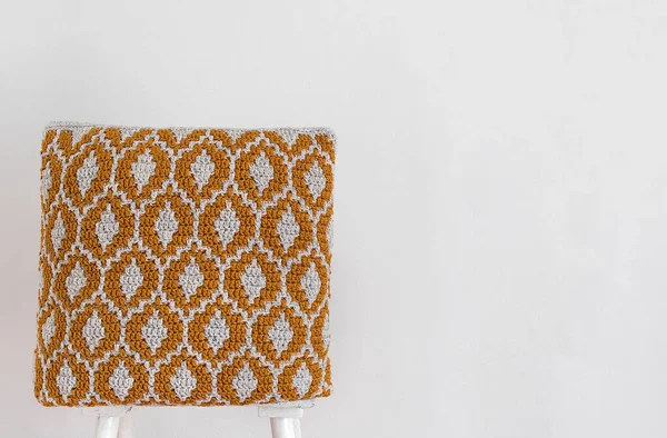 白い壁に対して椅子の上にオレンジ手作りのかぎ針編みの枕 抽象的なモザイク模様のクロシェクッション スペースのコピー — ストック写真