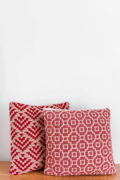 白い壁に対して木製のテーブルの上に2つの赤いかぎ針編みの枕 抽象的なモザイクパターンの手作りのかぎ針編みの枕 スペースのコピー — ストック写真