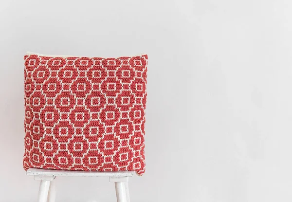 白い壁に対して椅子の上に赤いかぎ針編みの枕 抽象的なモザイクパターンのかぎ針編みの枕 スペースのコピー — ストック写真