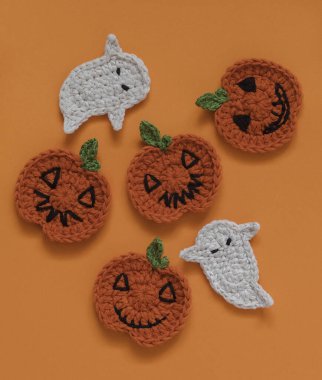 Turuncu arka planda örgü ören balkabakları ve hayaletli bayram kompozisyonu.