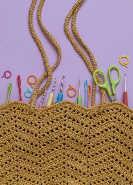 紫色の背部の明るいかぎ針編み用具が付いている黄色い網のかぎ針編み袋 ロイヤリティフリーのストック画像