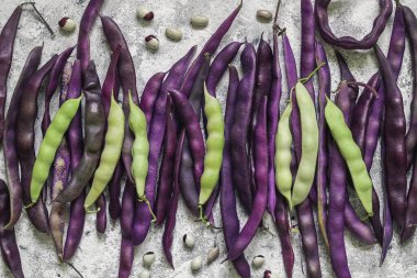 Birçok taze toplanmış mor ve yeşil fasulye kabukları bir masada. Üst görünüm.