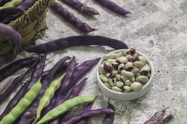 Bowl with fresh organic beans and purple bean pods on a table.