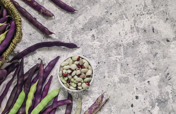 Bowl with fresh organic beans and purple bean pods on a table. Top view. Copy space.