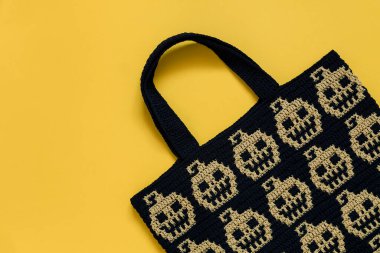 Sarı arka planda Cadılar Bayramı balkabaklarıyla el yapımı tığ işi çanta. Boşluğu kopyala.