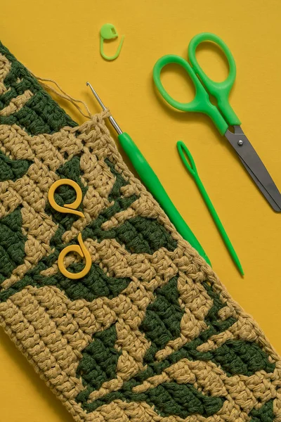 Yellow crochet fabric with green leaves and crochet tools on a yellow background.